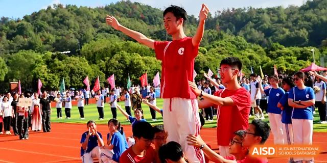 A student in a red shirt cheers enthusiastically with arms raised during a lively outdoor sports festival at Zhejiang ZhouShan High School.