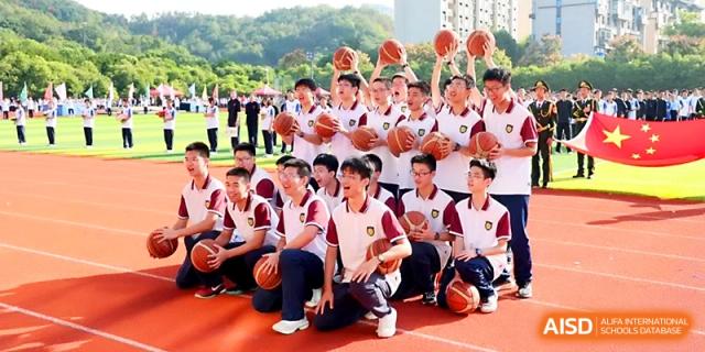 A large group of male students poses together on an outdoor court while holding basketballs for a team photo at Zhejiang ZhouShan High School.