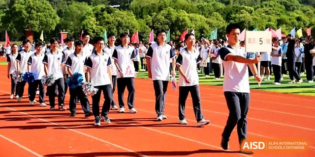 A line of students in white uniforms walks across the red running track during a formal athletic procession at Zhejiang ZhouShan High School.