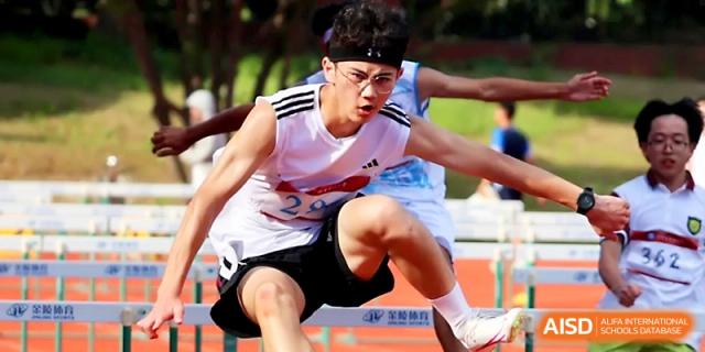 An athlete wearing a headband focuses intensely while leaping over a hurdle during a race at Zhejiang ZhouShan High School.
