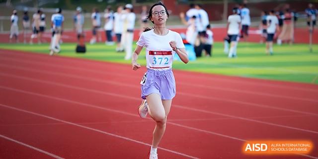 A female student in a white shirt and purple shorts runs with speed on the school track at Zhejiang ZhouShan High School.