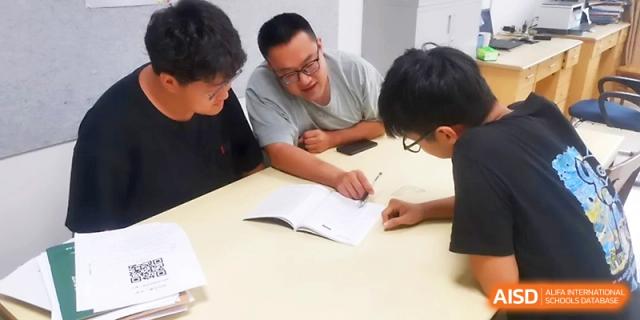 A teacher and two students review study materials together during a focused academic session in a classroom at Zhengzhou No.1 High School