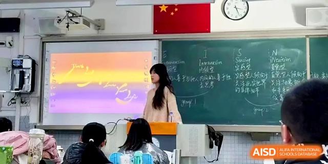 A female student stands at the front of the classroom presenting a lesson to her classmates near a projector at Zhengzhou No.1 High School