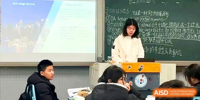 A female student standing at a classroom podium gives a presentation with a projector screen and chalkboard behind her at Zhengzhou No.1 High School