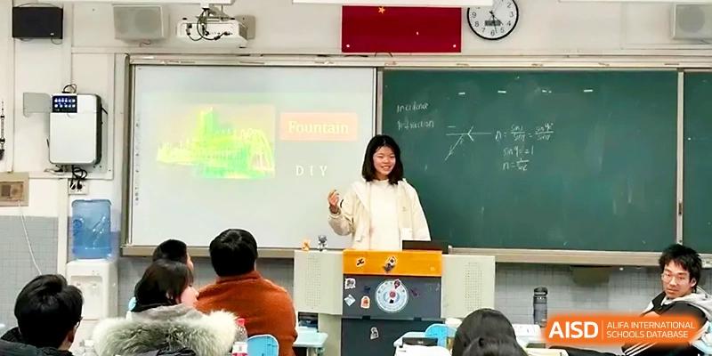 A student in a white jacket smiles while presenting a slide about tourism to the class at Zhengzhou No.1 High School