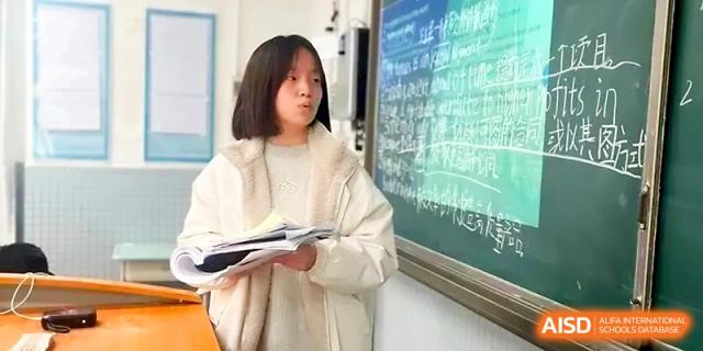 A student stands near a chalkboard filled with notes while holding study materials in a classroom at Zhengzhou No.1 High School