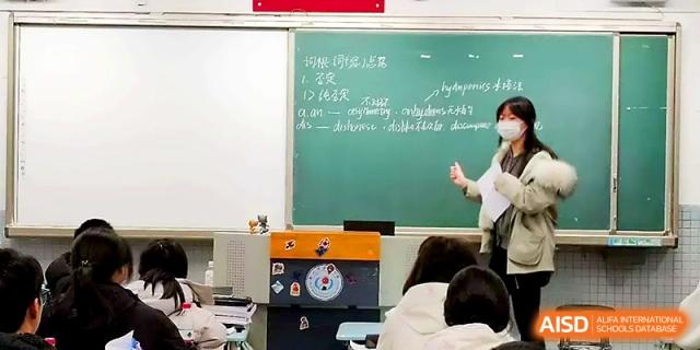 A teacher gestures toward a green chalkboard during a lecture to a classroom full of students at Zhengzhou No.1 High School