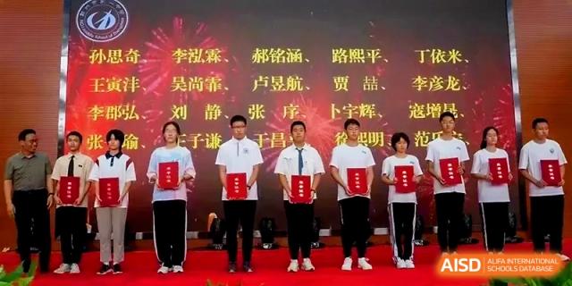 Four students stand on a red stage holding award certificates during a formal school ceremony at Zhengzhou No.1 High School