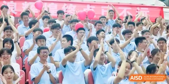 A large group of students in blue shirts cheers and claps during an energetic school assembly at Zhengzhou No.1 High School