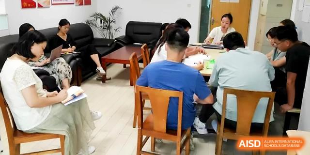A group of students and a teacher sit around a table for a collaborative meeting in an office at Zhengzhou No.1 High School