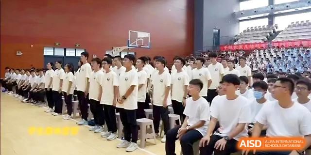 Rows of male students in white shirts stand at attention during an indoor school assembly or event at Zhengzhou No.1 High School