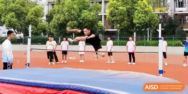 A male student performs an athletic high jump maneuver over a horizontal bar on the school sports field at Zhengzhou No.1 High School