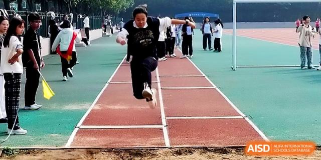 A student athlete performs a long jump landing in the sand pit during an outdoor physical education competition at Zhengzhou No.1 High School