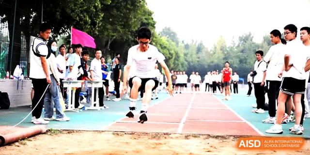 An athlete wearing a white shirt completes a long jump landing with great focus during a track event at Zhengzhou No.1 High School