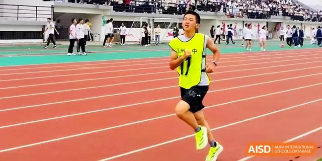 A runner in a neon yellow vest sprints across the red athletic track during a school-wide sports festival at Zhengzhou No.1 High School