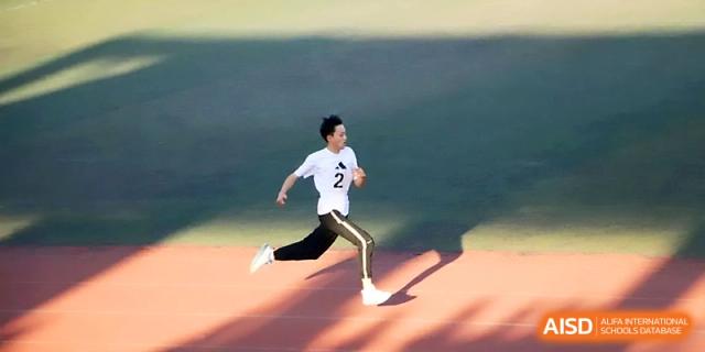 A student athlete in a white shirt sprints with determination across the open athletic field during a race at Zhengzhou No.1 High School