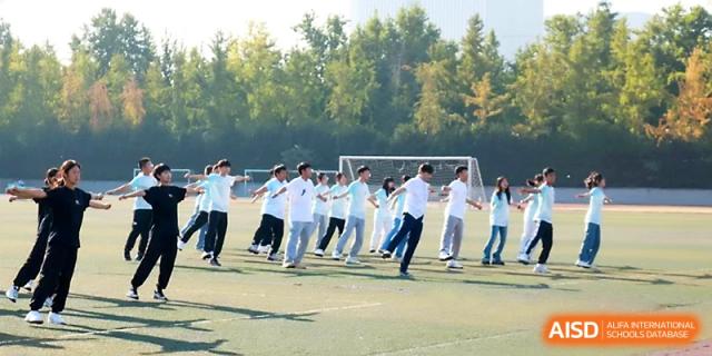 A wide shot of students in white uniforms participating in a synchronized exercise routine on the green field at Zhengzhou No.1 High School