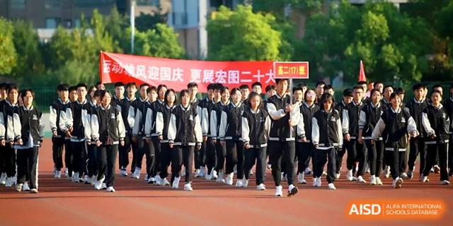 A large formation of students in uniform marches across the red running track during an opening ceremony at Zhengzhou No.1 High School