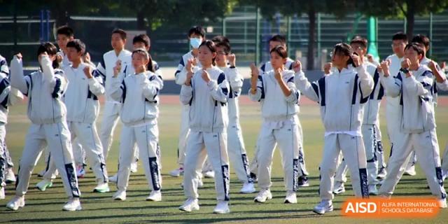 Students in matching white and grey tracksuits stand together on the athletic field during a formal ceremony at Zhengzhou No.1 High School