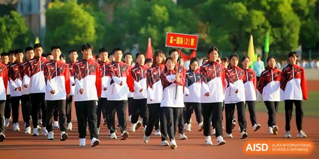 A disciplined group of students marches in rows while carrying flags and signs during a sports parade at Zhengzhou No.1 High School