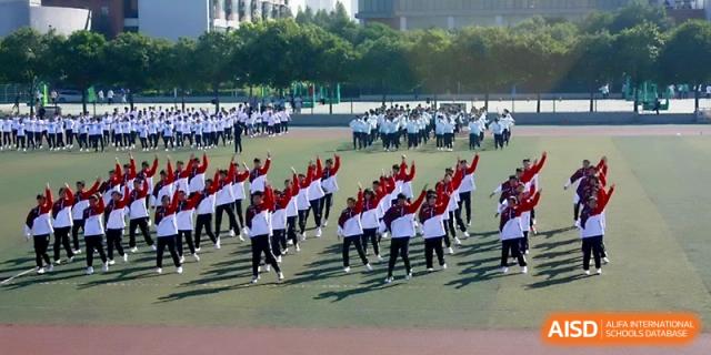 A high-angle view of a massive group of students performing synchronized calisthenics on the sports field at Zhengzhou No.1 High School