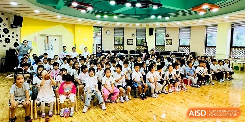 A large group of children sit attentively on the floor of a bright and colorful activity room for a lesson at Zhengzhou No.1&8 United International School