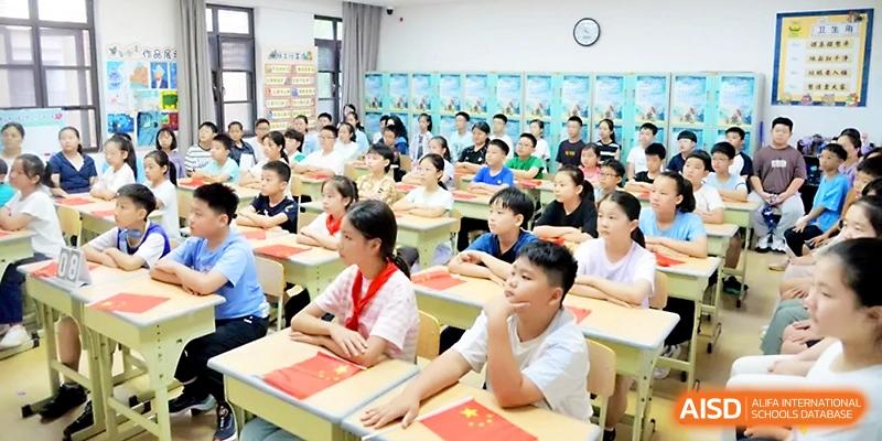 A classroom full of students in white uniforms sits attentively at their desks during a primary school lesson at Zhengzhou No.1&8 United International School