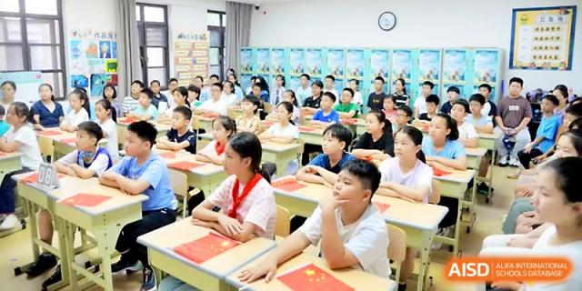 A classroom full of students in white uniforms sits attentively at their desks during a primary school lesson at Zhengzhou No.1&8 United International School