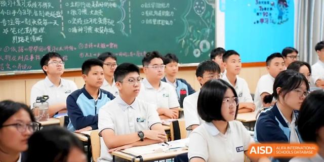 Students in white polo shirts focus on their teacher during a lesson in a classroom with a green chalkboard at Zhengzhou No.1&8 United International School