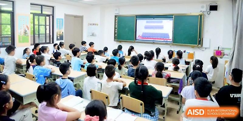 Primary students sit in a bright classroom while watching an educational presentation on a wall-mounted digital screen at Zhengzhou No.1&8 United International School