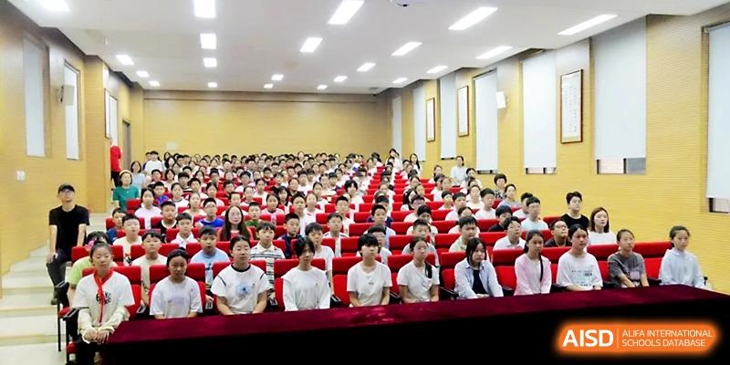 A large audience of students fills an auditorium with red seating for a formal academic lecture or event at Zhengzhou No.1&8 United International School