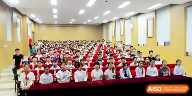 A large audience of students fills an auditorium with red seating for a formal academic lecture or event at Zhengzhou No.1&8 United International School