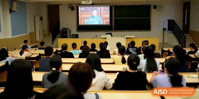 An audience of students sits in a darkened lecture hall watching a video presentation on a large theater screen at Zhengzhou No.1&8 United International School