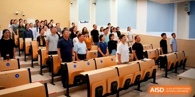 A large group of adults stands in a lecture hall for a formal presentation or meeting during a campus event at Zhengzhou No.1&8 United International School