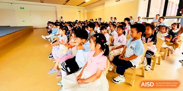 A row of young children in school uniforms sits together during an assembly or special performance on campus at Zhengzhou No.1&8 United International School