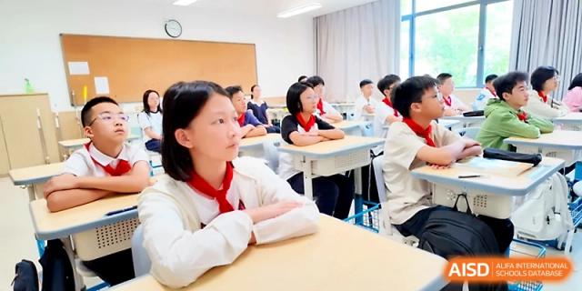 A female student with a red scarf sits at her desk with a thoughtful expression during a classroom lesson at Zhengzhou No.1&8 United International School
