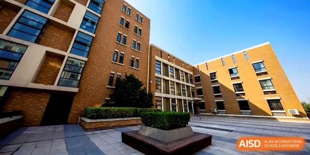 A low-angle shot of a grand brick school building with multiple levels and large windows on a sunny day at Zhengzhou No.1&8 United International School