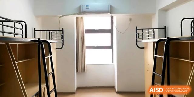 A simple and clean dormitory room with a window, white walls, and a metal bed frame for student living at Zhengzhou No.1&8 United International School