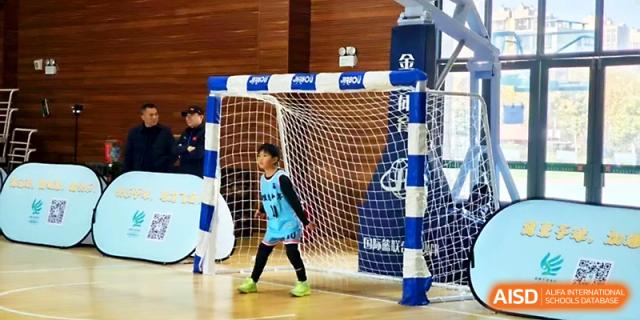 A young goalkeeper in a blue jersey stands ready in front of a soccer net during a match at Zhengzhou No.1&8 United International School