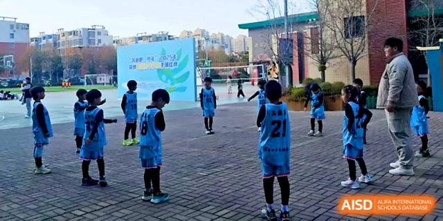 Young basketball players in numbered jerseys practice their coordination on an outdoor court at Zhengzhou No.1&8 United International School