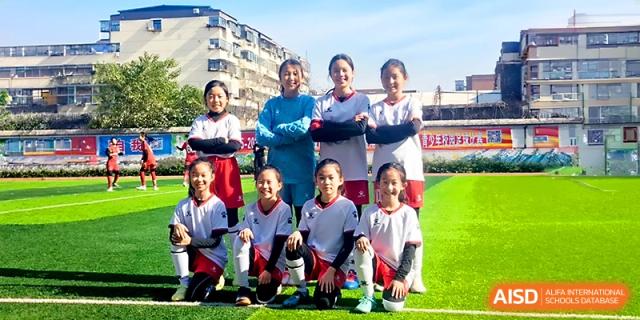 A girls' soccer team in red and white uniforms poses for a group photo on the green field at Zhengzhou No.1&8 United International School