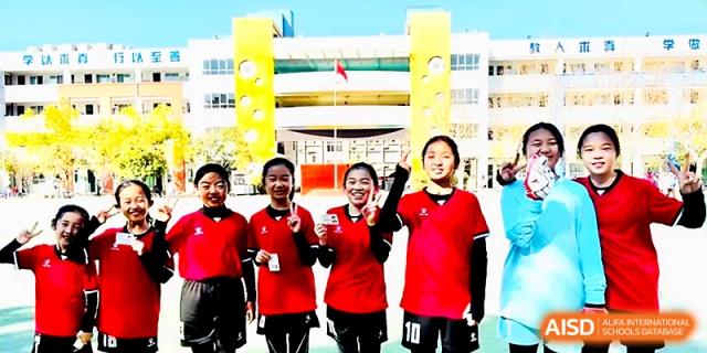 Four female students in red sports uniforms smile brightly while standing on the athletic field at Zhengzhou No.1&8 United International School