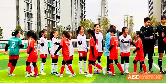A group of young soccer players in red and white uniforms gathers on the green turf at Zhengzhou No.1&8 United International School