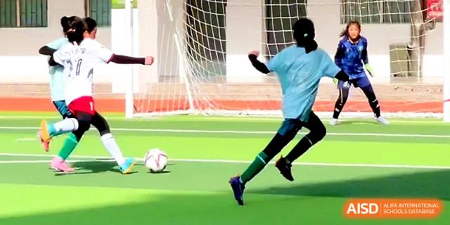 A student in a light blue jersey runs toward the soccer ball during an outdoor match at Zhengzhou No.1&8 United International School