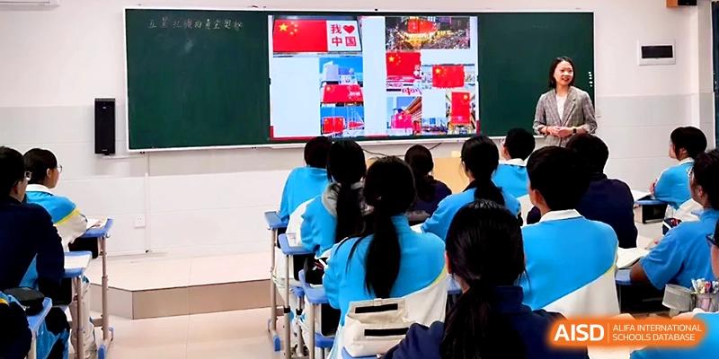 Students in blue uniforms sit in a classroom watching a digital presentation about national symbols and history at Zhengzhou No.4 Middle School