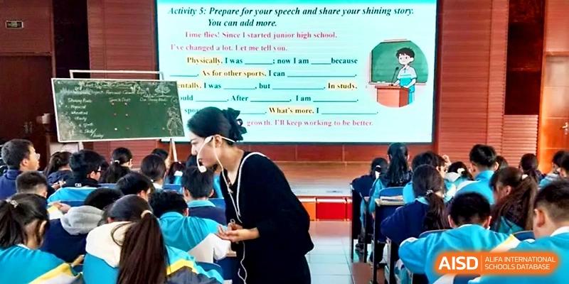 A teacher assists students during an English language lesson featuring a presentation on public speaking at Zhengzhou No.4 Middle School