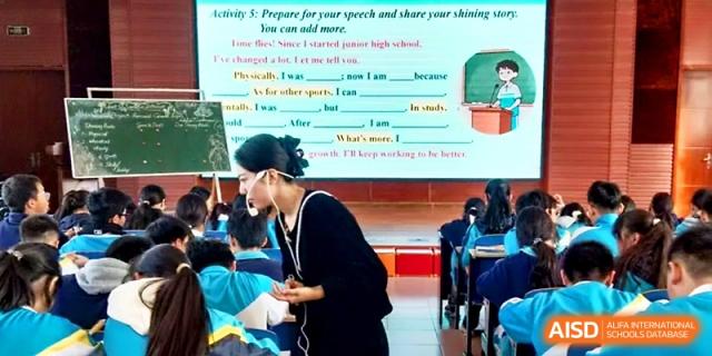 A teacher assists students during an English language lesson featuring a presentation on public speaking at Zhengzhou No.4 Middle School