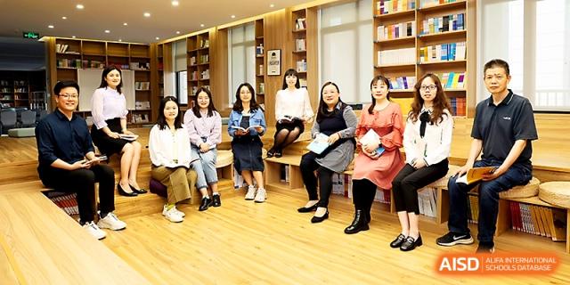 A group of female faculty members sits together in a modern, wood-paneled school library or lounge at Zhengzhou No.4 Middle School