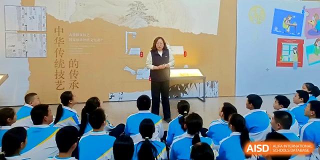 A presenter speaking to a large group of students in a lecture hall at Zhengzhou No.4 Middle School.