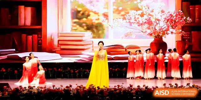 A soloist in a flowing yellow gown performs on a grand stage with a choir behind her during a formal event at Zhengzhou No.4 Middle School.
